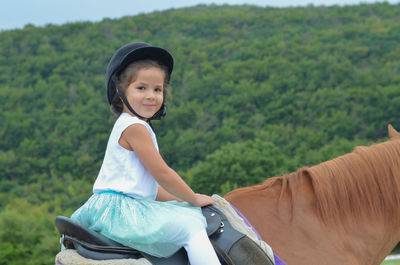 Happy girl riding horse against mountain