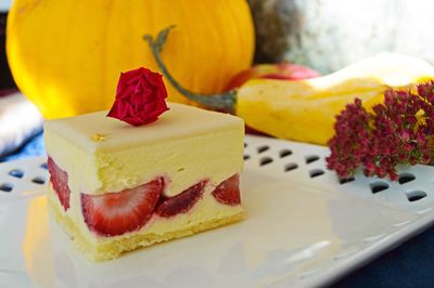 Close-up of strawberry cream cake with pumpkin in background
