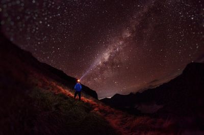 Rear view of man with illuminated flashlight on field against sky at night