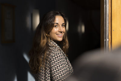 Smiling woman with long hair looking over shoulder at apartment entrance