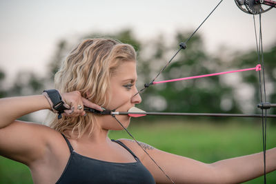 Close-up of young woman aiming bow at park