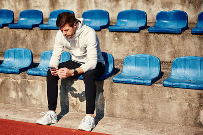 Man in sportswear resting at stadium seat and use smartphone