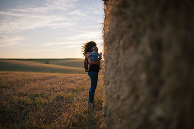 Mother carrying daughter while standing on field against sky