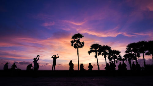 Silhouette people and palm trees against dramatic sky during sunset