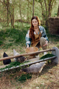 Smiling woman feeding hen at farm