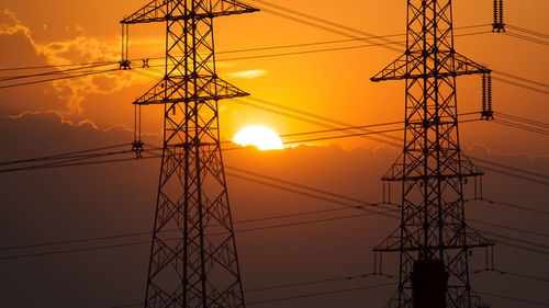 Low angle view of electricity pylon against sky during sunset