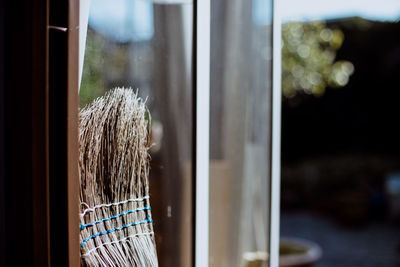 Close-up of garden broom leaning at glass window