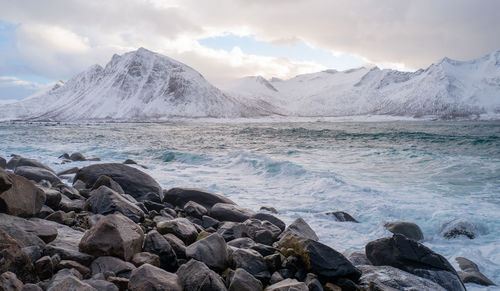 Scenic view of sea by snowcapped mountains against sky