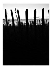 Silhouette wooden posts on beach against sky