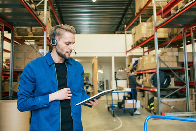 Confident manual worker wearing headphones while using digital tablet in warehouse