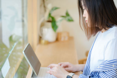 Side view of young woman using laptop at table
