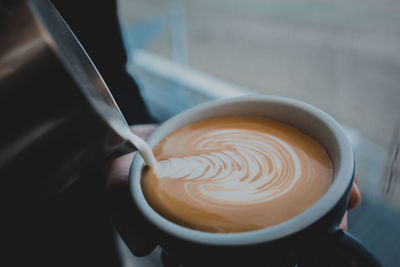 Close-up of hand pouring milk in coffee