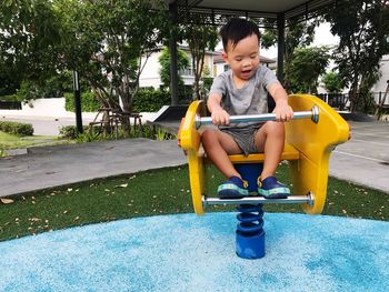 Full length of smiling boy sitting on slide at park