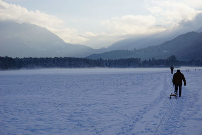 Man carrying sled on snow covered field