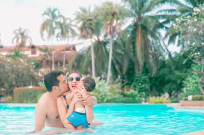 Father and daughter in swimming pool against trees