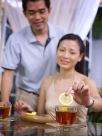 Woman with man adding lemon slice in tea on glass table at home