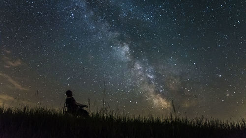 Low angle view of person sitting on field against star field