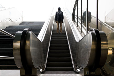 Low angle view of man carrying backpack standing on escalator