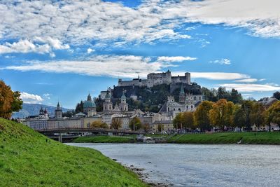 View of castle by river against cloudy sky