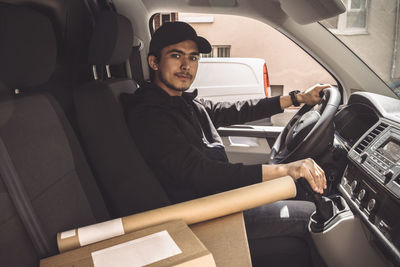 Portrait of confident delivery man with package driving truck