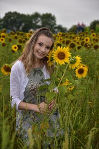 Portrait of smiling teenage girl with sunflowers standing on field