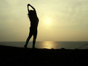 Silhouette of woman standing on beach at sunset