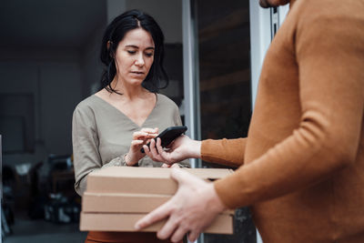 Woman receiving parcel and signing on smart phone at doorway