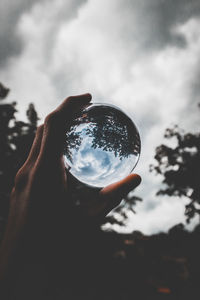 Cropped image of hand holding crystal ball against sky