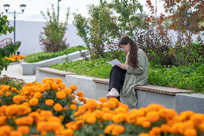 A girl sits on a bench on the street with documents in her hands and using her phone