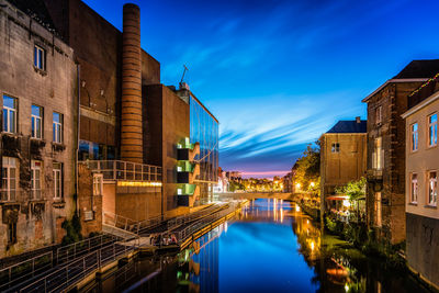 Canal amidst buildings in city against sky at dusk