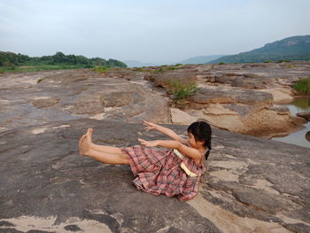 Girl sitting on rock against sky