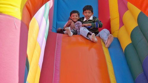 Portrait of smiling brothers sitting on colorful inflatable outdoor play equipment