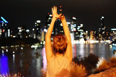 Rear view of woman against river in city at night