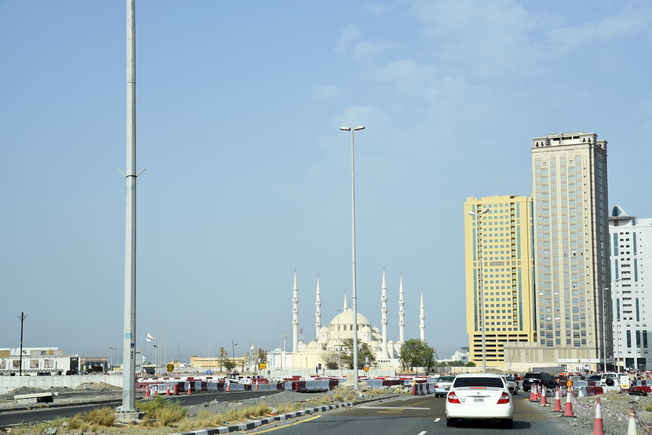 CARS ON ROAD BY BUILDINGS AGAINST SKY