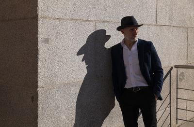 Portrait of adult man in hat and suit standing on street against wall. madrid, spain