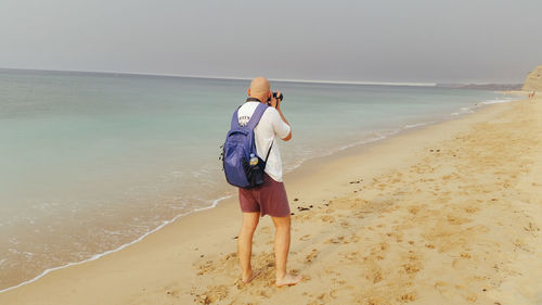 Rear view of mid adult man photographing on shore at beach