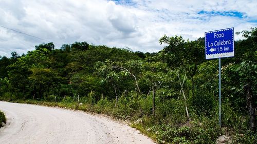 Road sign by trees against sky