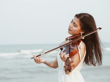 Woman playing violin by sea against clear sky