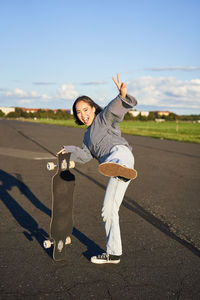 Side view of young woman standing on road against sky