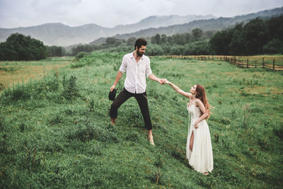 Full length of young couple holding hands while standing on grassy field