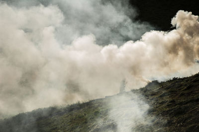 Old woman seen as a silhouette through the back-lit smoke as she is racking the sear burned grass