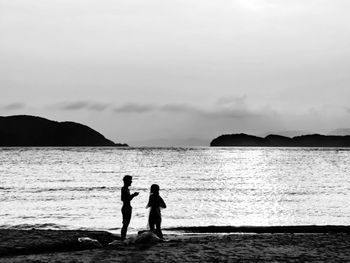 Silhouette women standing on beach against sky