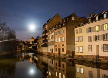 Buildings by lake against sky at night