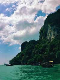 Scenic view of green mountain by sea against cloudy sky