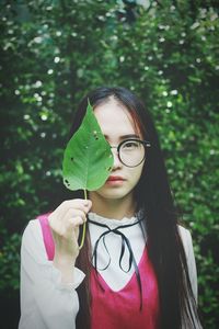 Portrait of young woman holding leaf in front of face
