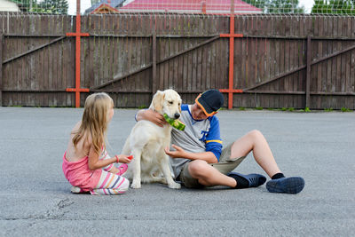 Siblings feeding golden retriever with watermelon on road