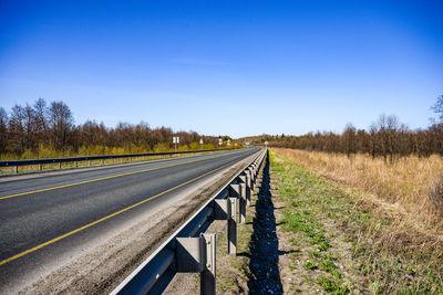 Empty road on field against clear blue sky