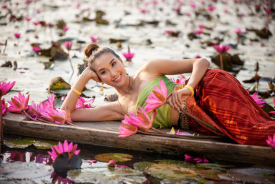 Portrait of woman lying on boat by pink lotus in lake
