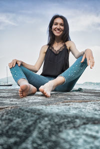 Portrait of smiling young woman sitting against sky