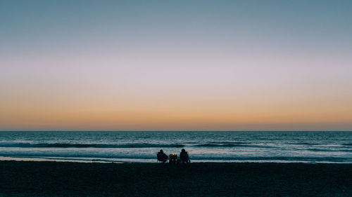 Silhouette people on beach against clear sky during sunset